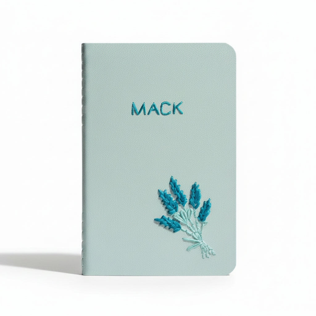 Light blue notebook with 'MACK' embroidered on it and lavender design, on a white background