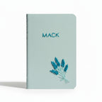 Light blue notebook with 'MACK' embroidered on it and lavender design, on a white background