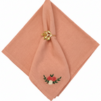 Pink napkin with floral embroidery and a gold napkin ring on a white background
